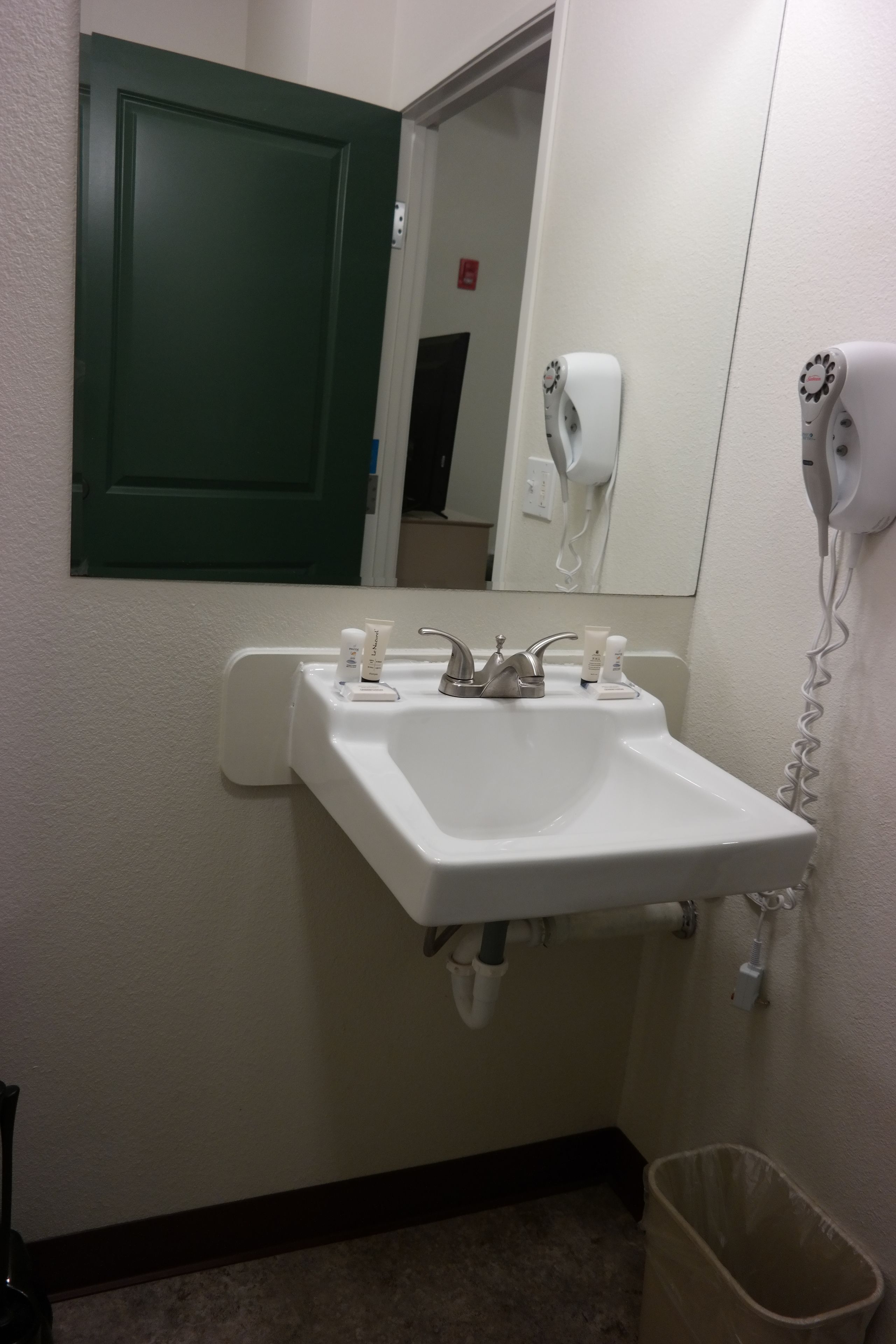 A bathroom with a white sink, a green door, a hand dryer, and a trash can.
