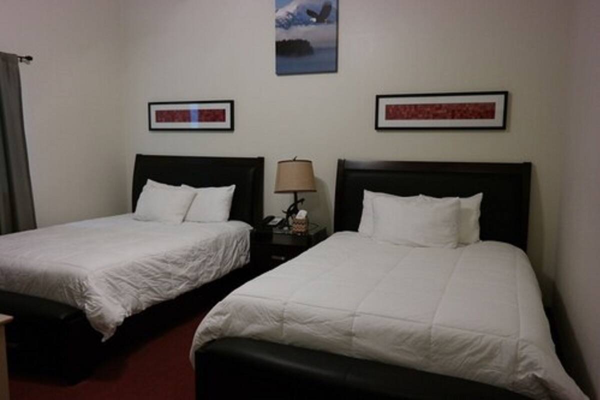 Habitación de hotel con dos camas individuales, una mesita de noche con lámpara y dos cuadros enmarcados en la pared.