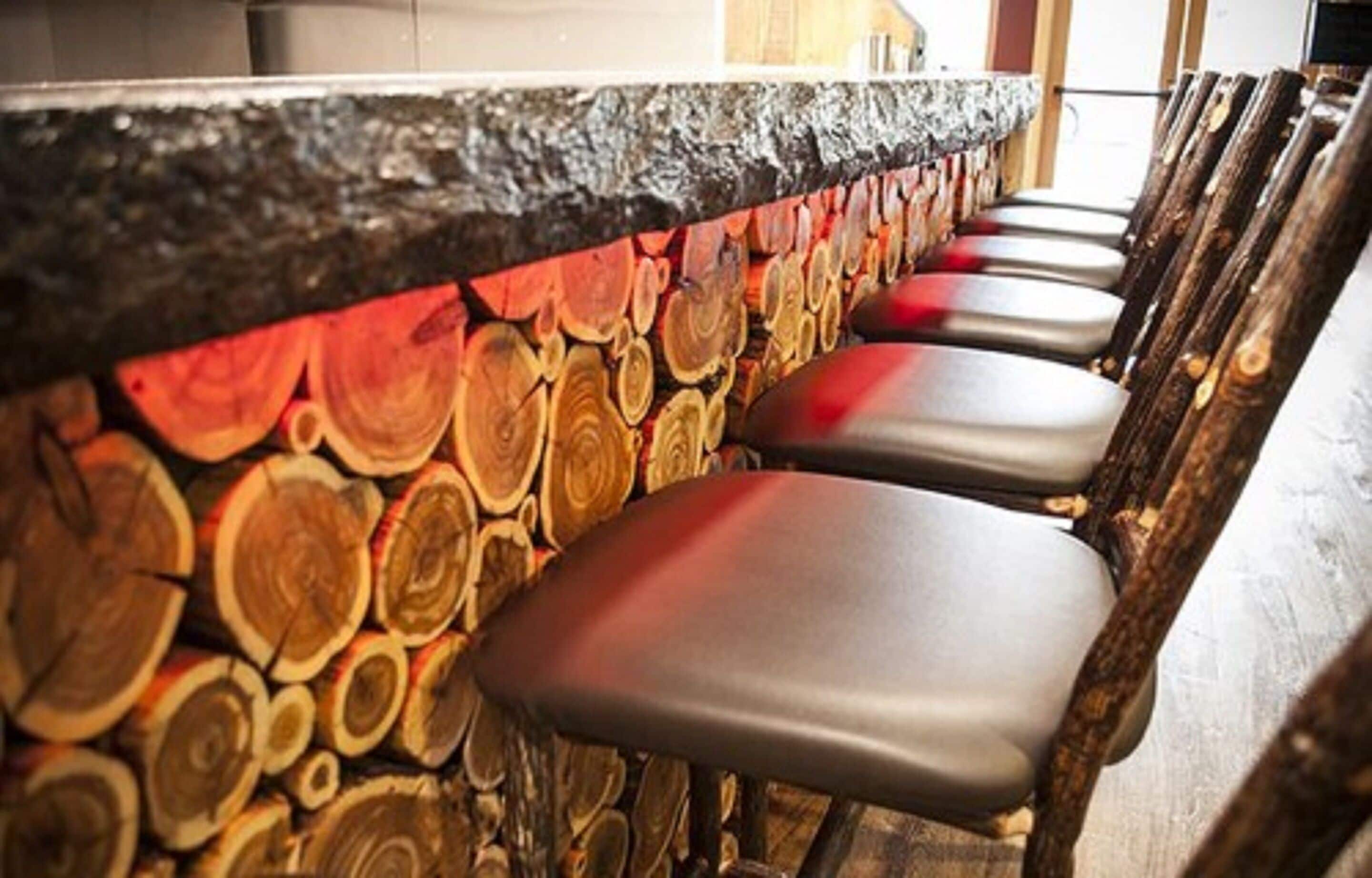 A bar area with a rustic wooden wall and several cushioned bar stools.