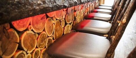 A bar area with a rustic wooden wall and several cushioned bar stools.