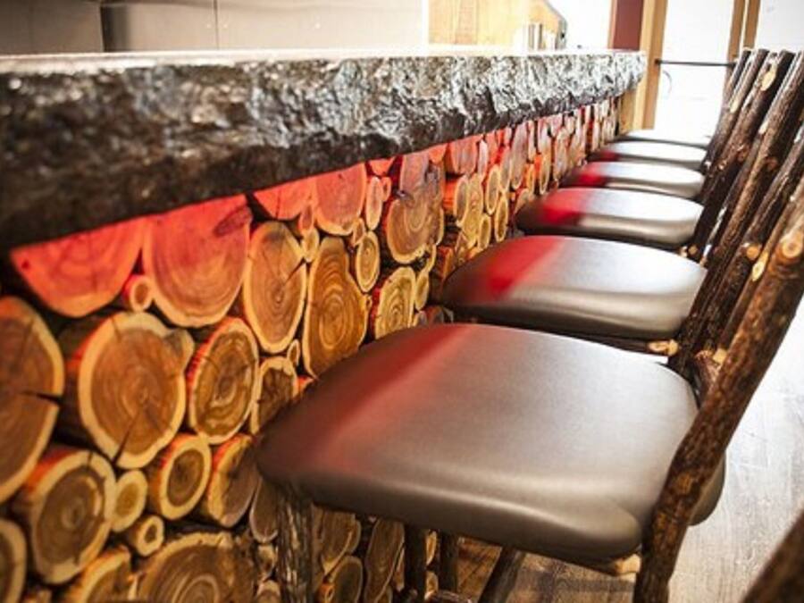 A bar area with a rustic wooden wall and several cushioned bar stools.