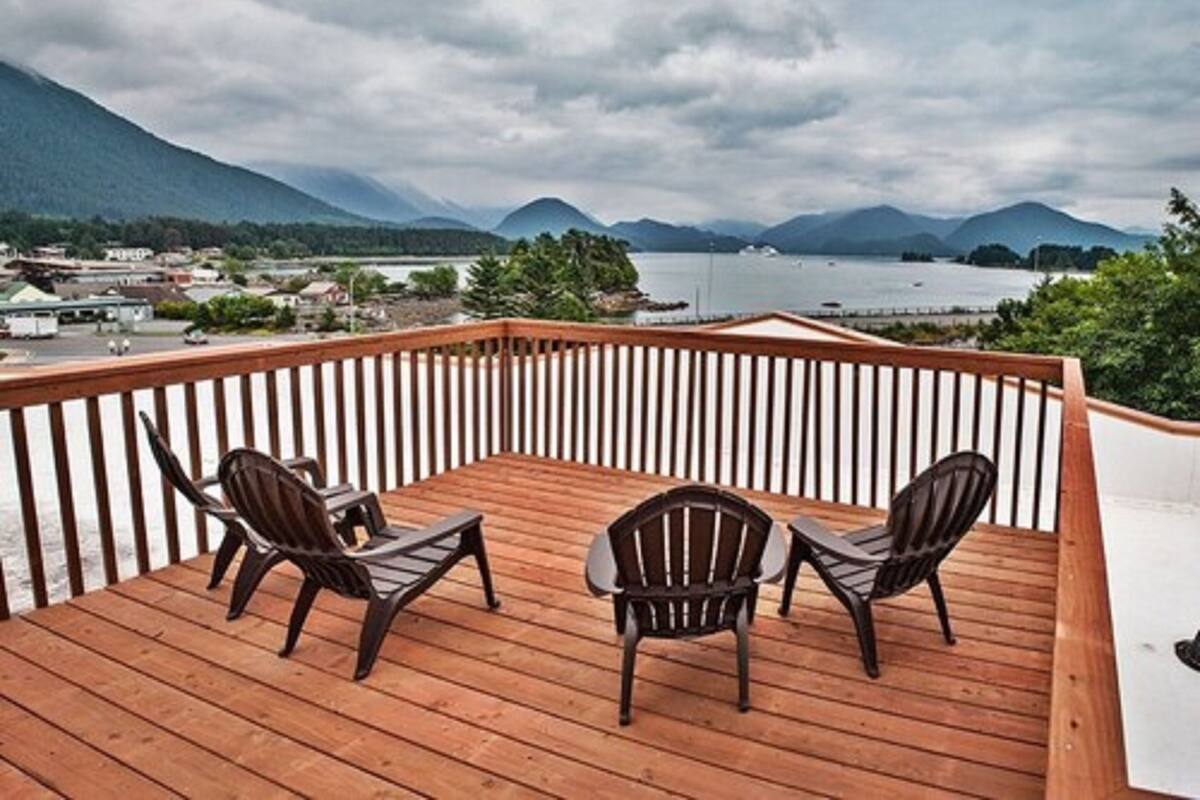 Una terraza de madera con dos sillas Adirondack mirando un paisaje con montañas y un lago.