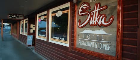 The Sikka Hotel with a wooden facade, large signage, and windows advertising cocktails and bar services.