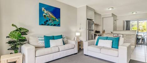 A modern living room with two white sofas, a large painting of a sea turtle, and a potted plant.