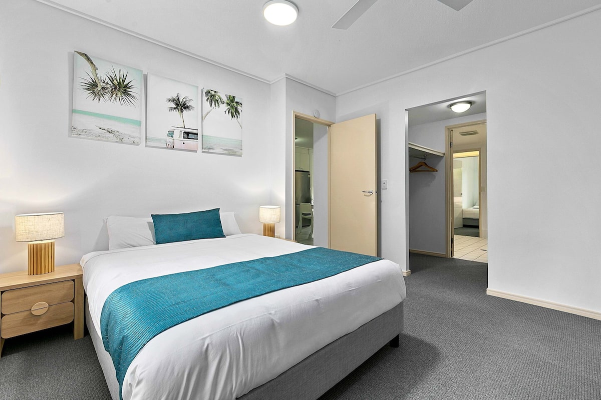 Un dormitorio ordenado con cama, mesitas de noche y cuadros en la pared.