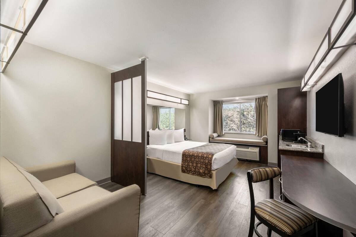 A compact hotel room with a bed, a seating area, a desk, and a TV.