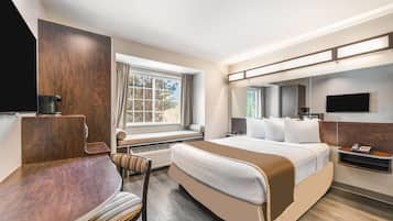 A hotel room with a bed, a desk, a chair, a TV, and a window with curtains.