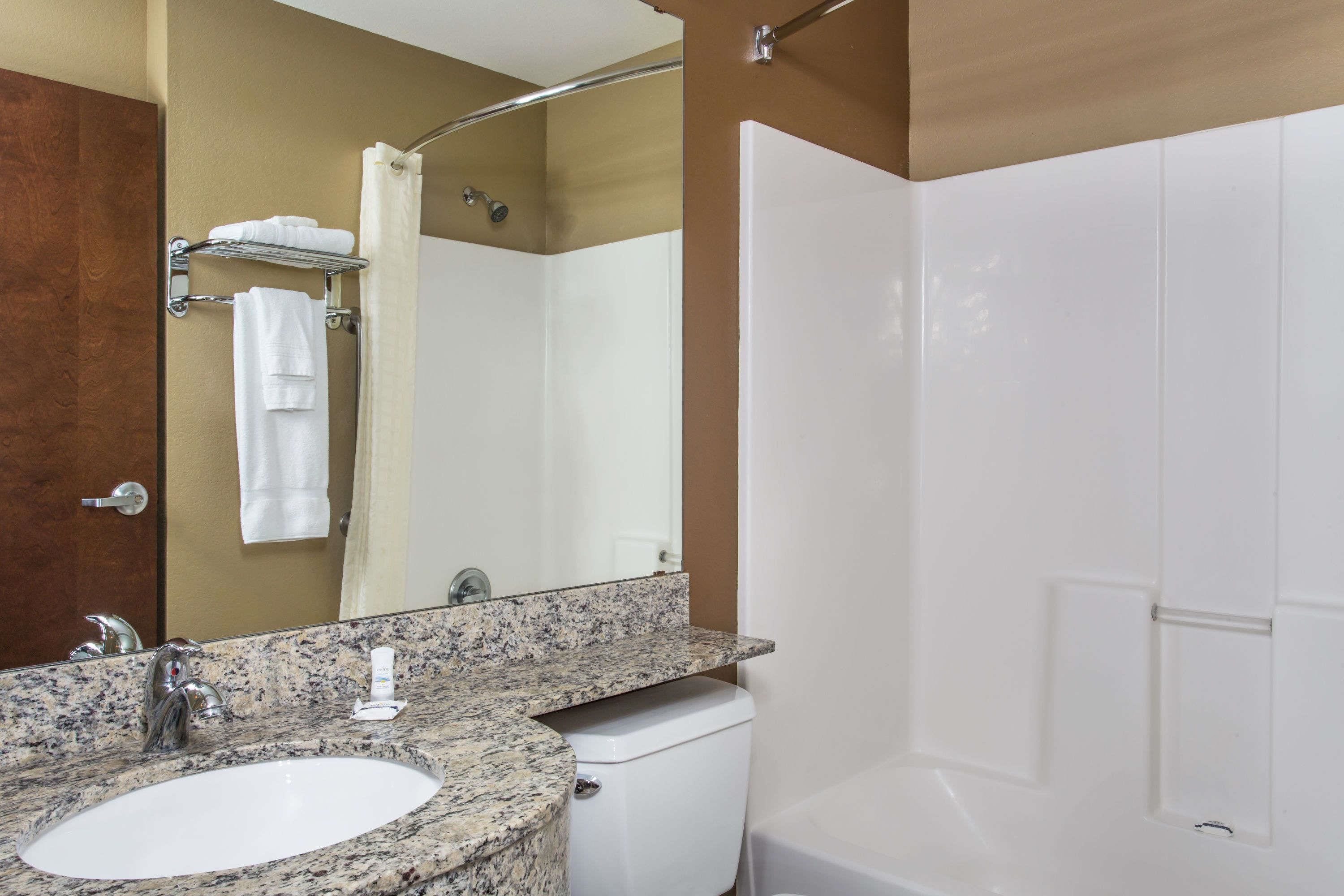 A bathroom with a granite sink, a toilet, a shower, and a mirror.