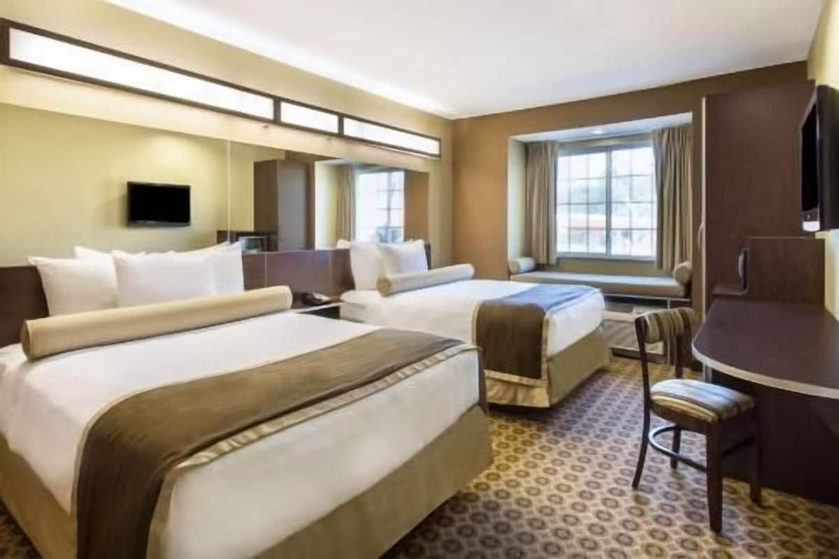 A hotel room with two beds, a desk, a chair, a TV, and a window with curtains.