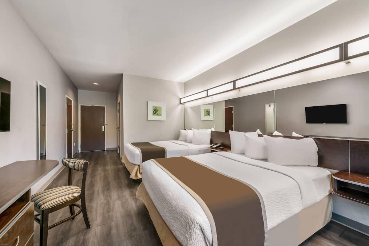 A hotel room with two beds, a desk, a chair, and a large mirror.