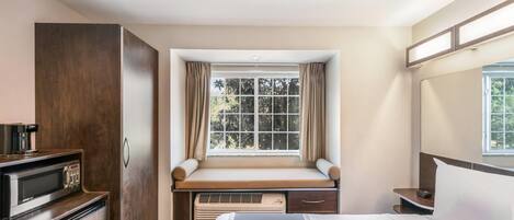 Habitación de hotel con cama, escritorio integrado con microondas, calefacción y ventana con cortinas.