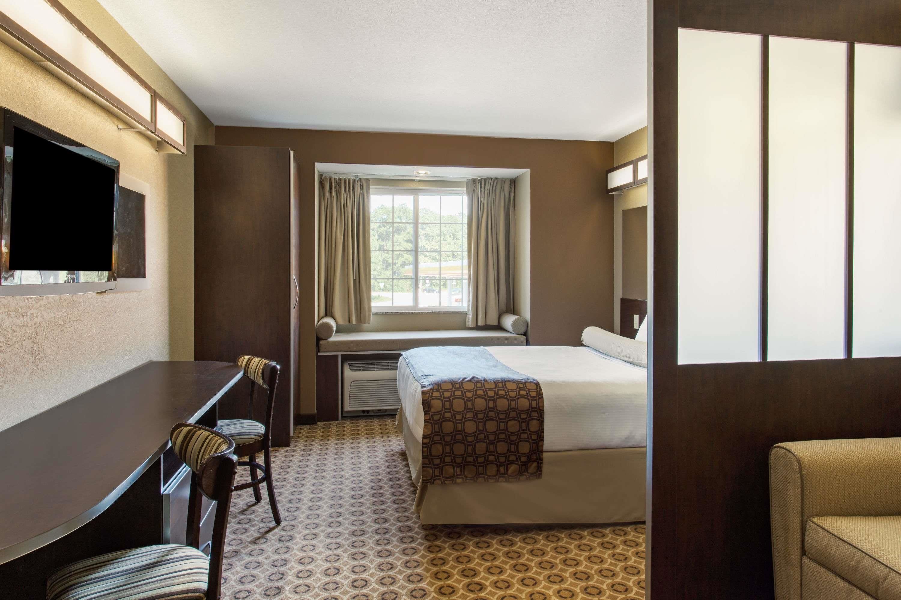 Ein Hotelzimmer mit Bett, Schreibtisch mit zwei Stühlen, einem Vorhangfenster und einem an der Wand montierten Fernseher.