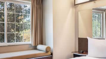 Une chambre d’hôtel avec un lit, une table de chevet, une fenêtre avec des rideaux et une vue sur les arbres à l’extérieur.