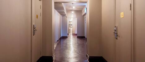 A long, narrow hallway with wooden flooring and white walls. There are doors on both sides, and a light fixture hangs from the ceiling.