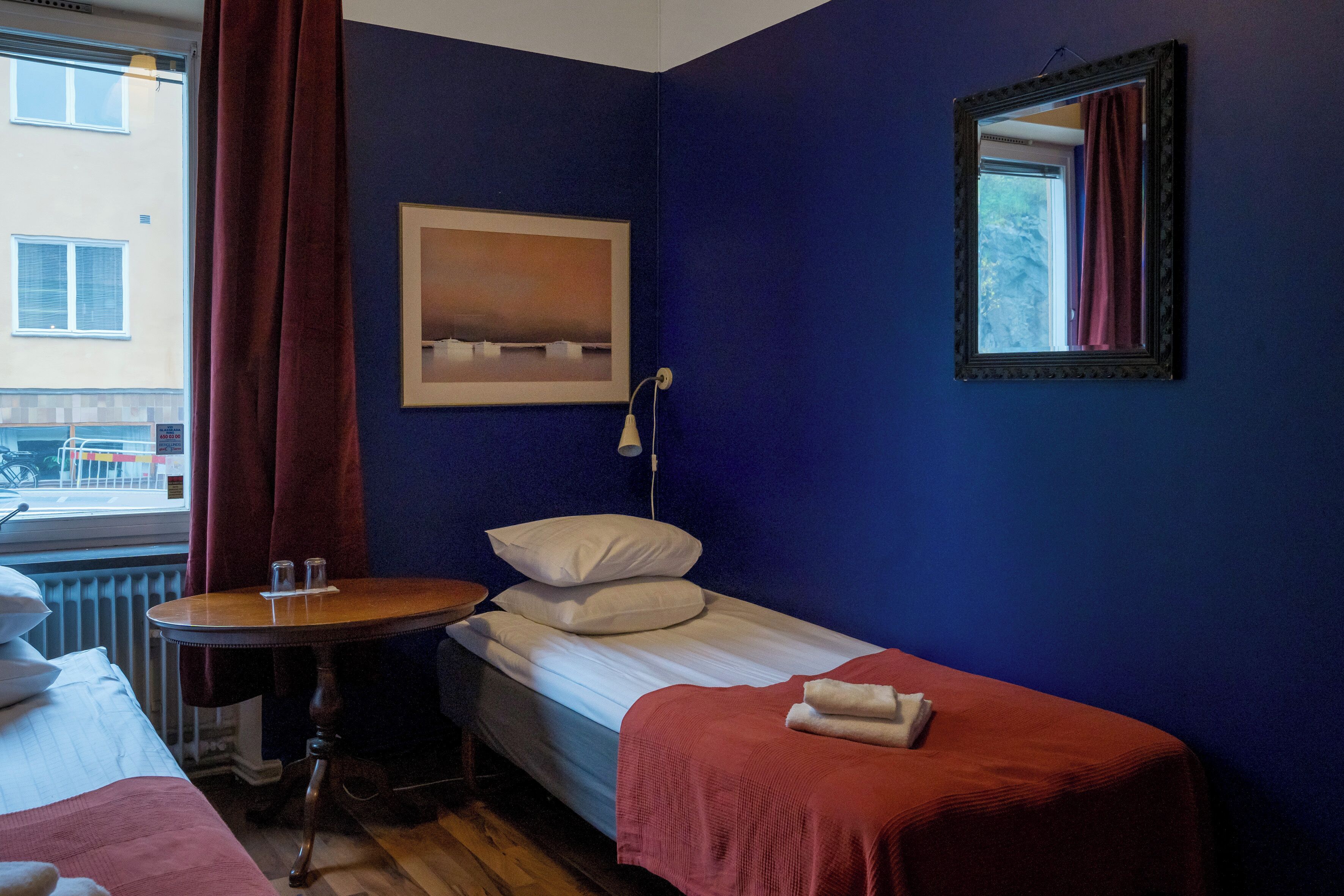 A small, neatly arranged room with a single bed, a small table, and a window with curtains.