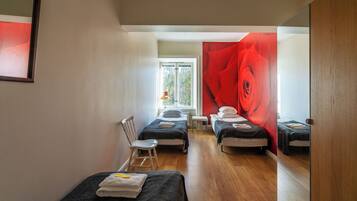 Una habitación con dos camas individuales, una mesita pequeña, una silla y un ventanal grande.