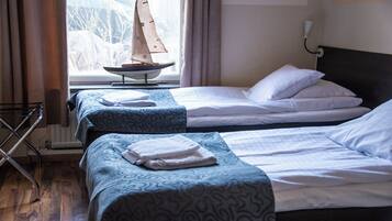 A hotel room with two beds, a window with a view of trees, a small sailboat model, and a radiator.