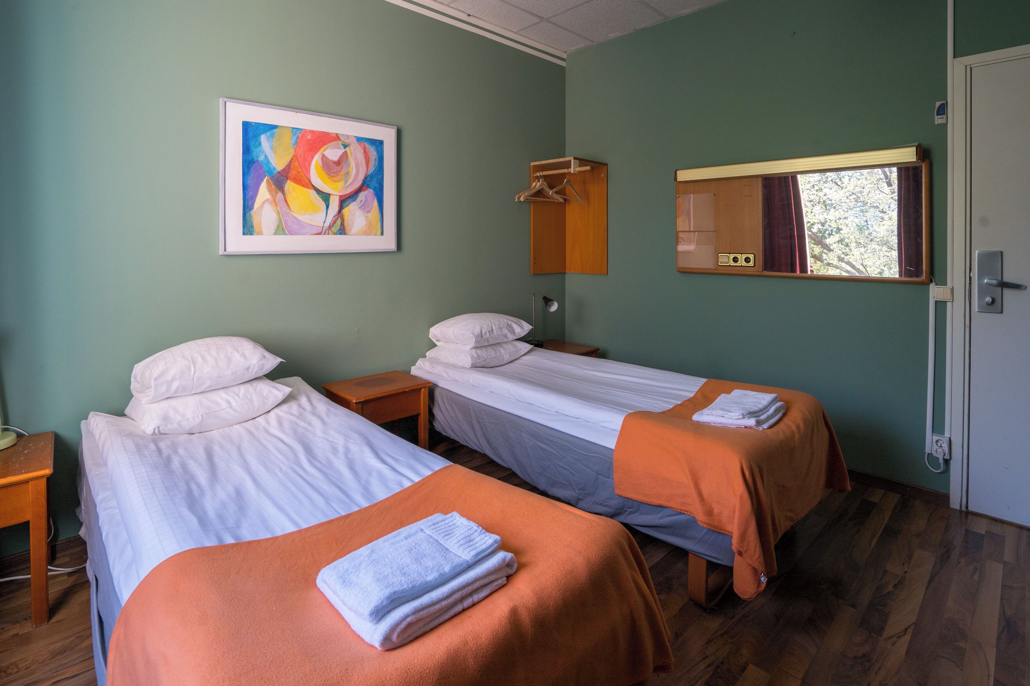 A room with two beds, a painting on the wall, a mirror, and a door.