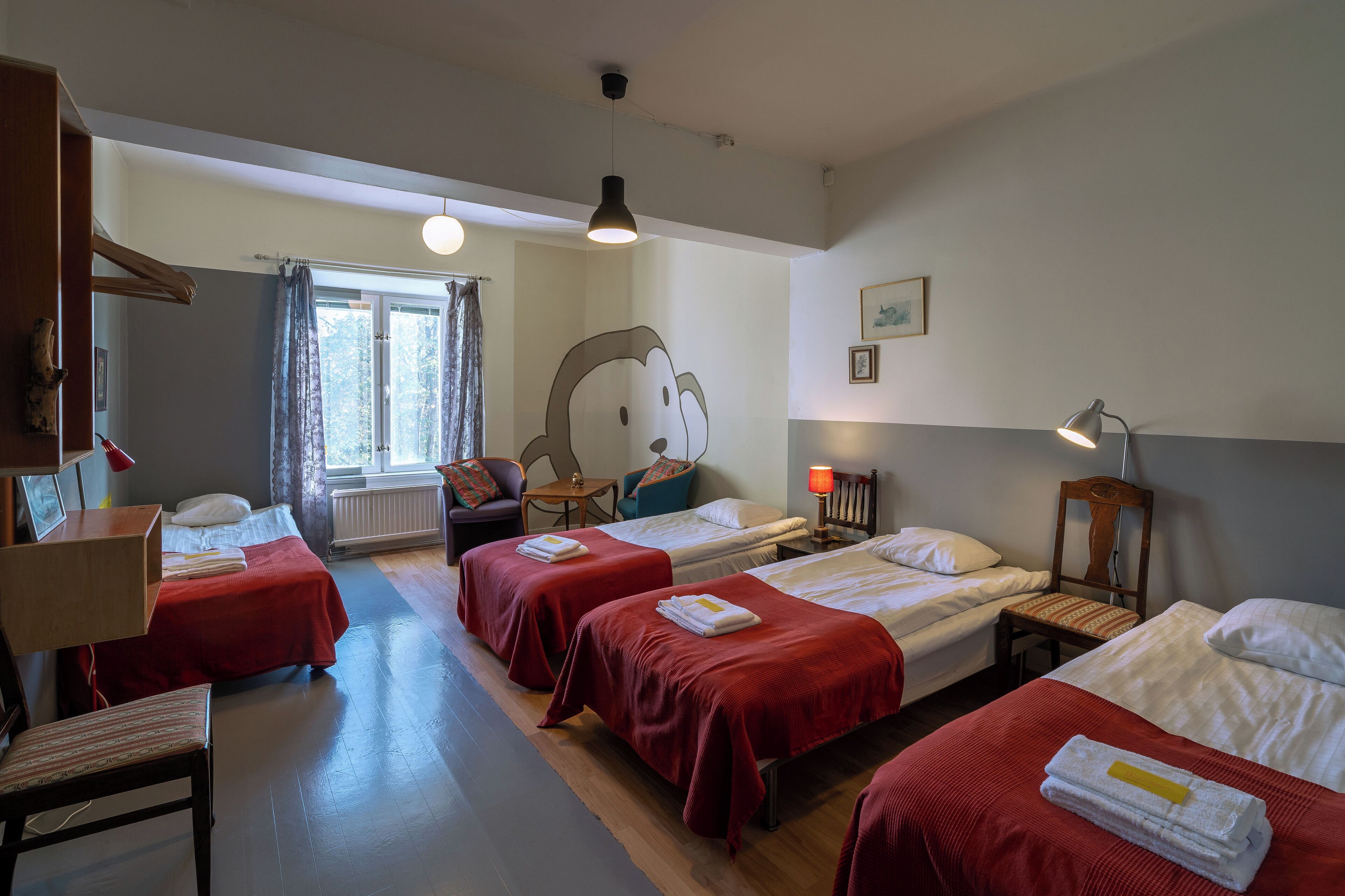 Una habitación de hotel con cuatro camas individuales, un escritorio, una silla, una ventana con cortinas, una lámpara y un adorno en la pared.