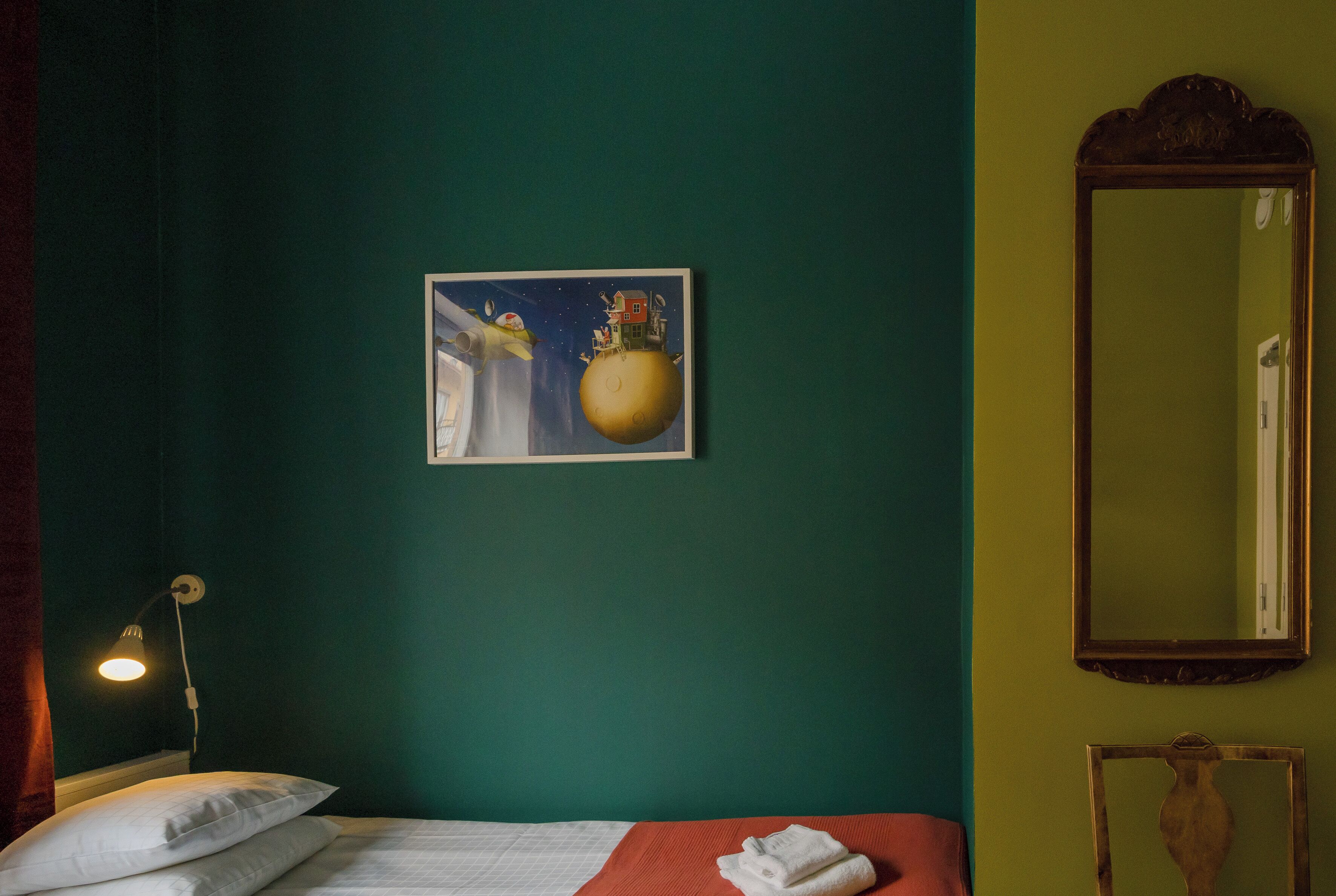 A room with a bed, a painting of a flying house, a mirror, and a lamp.