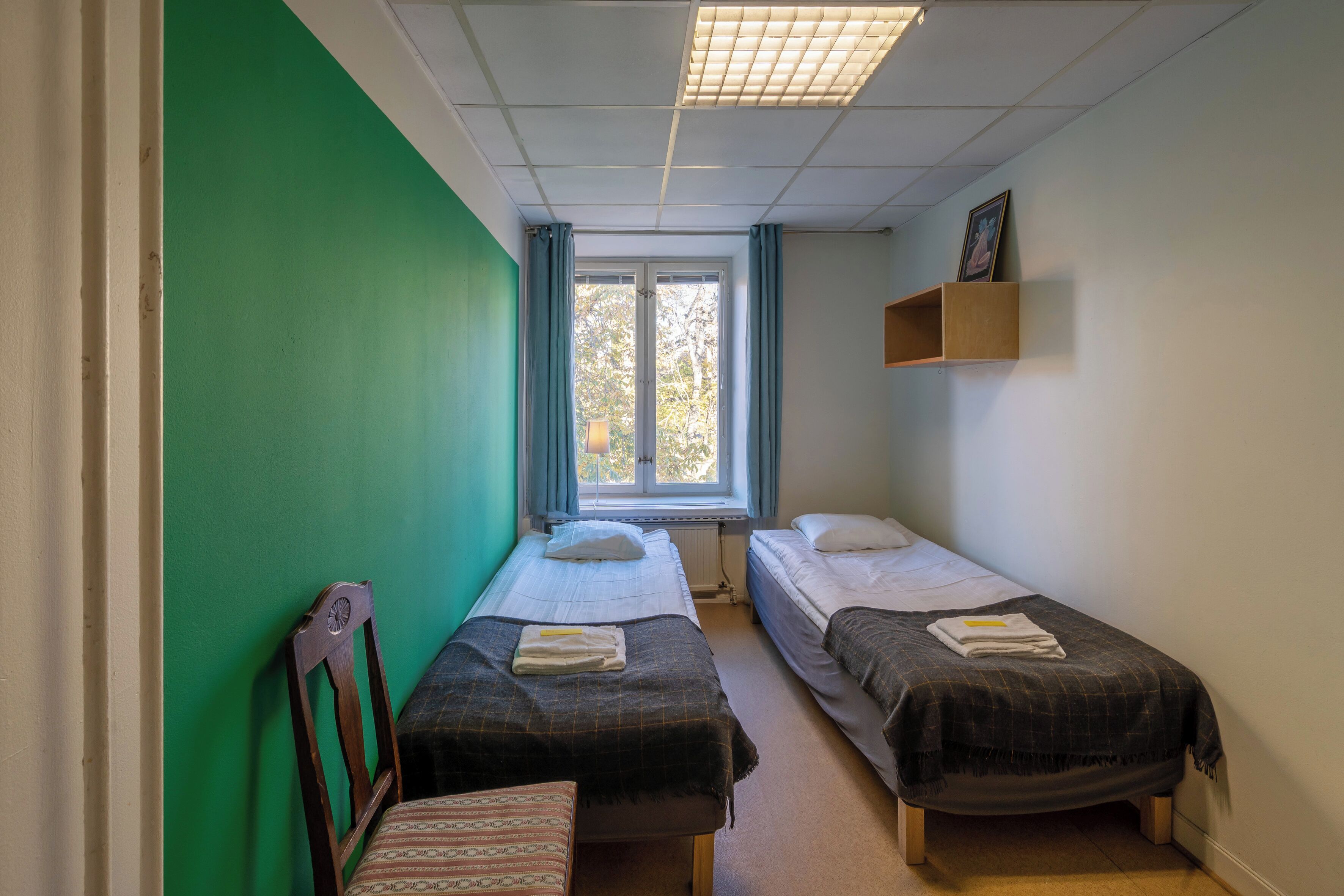 Een kamer met twee enkele bedden, een groene wand, een raam met gordijnen en een radiator.