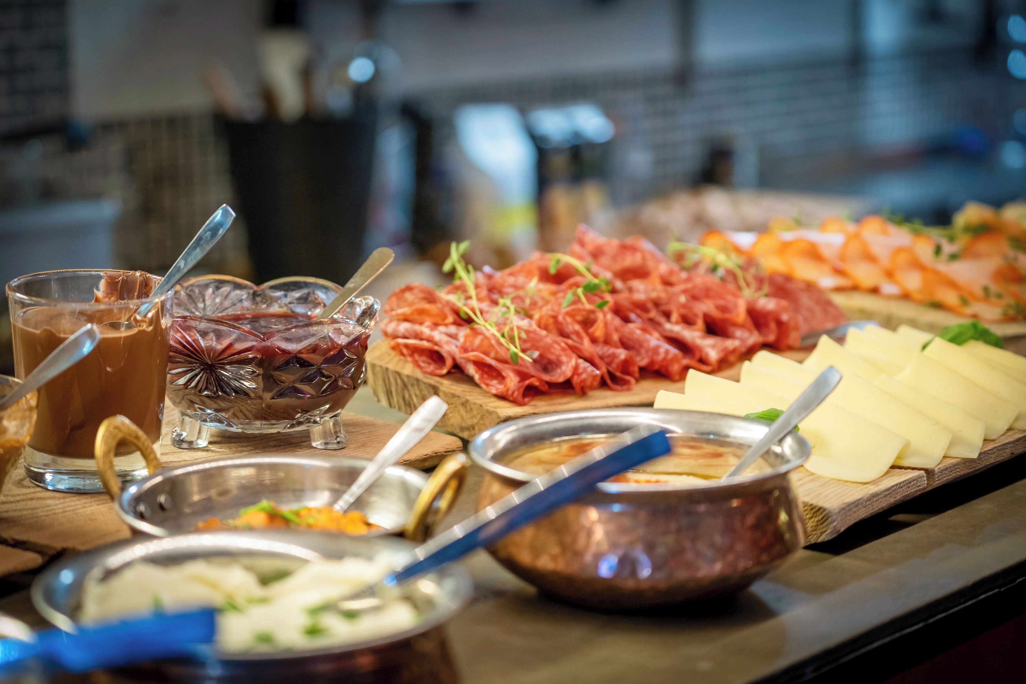 A buffet with various food items including meats, cheeses, and a hot beverage.