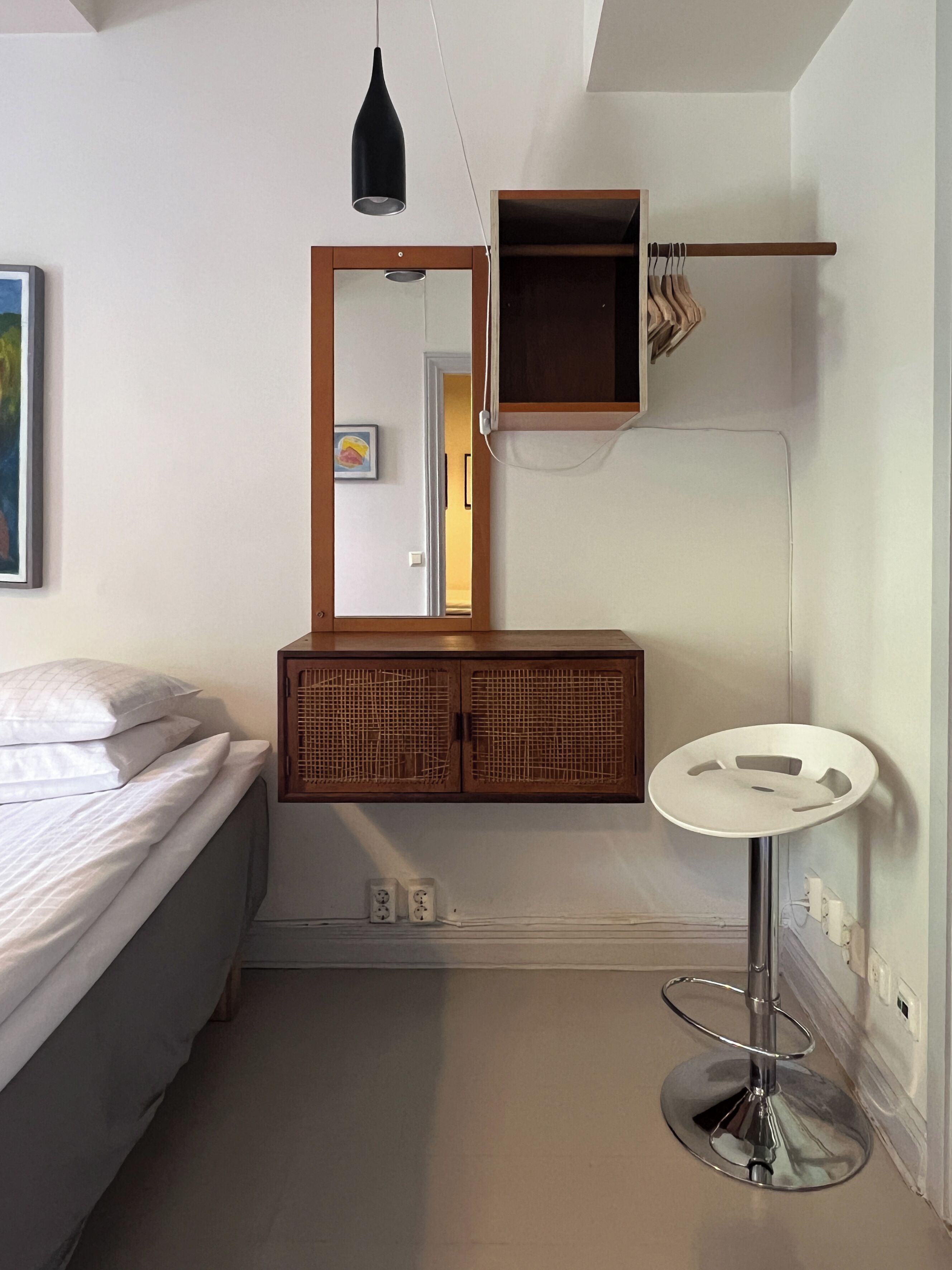 Un dormitorio con cama, mesita de noche, espejo, armario y una pequeña mesa redonda con taburete.