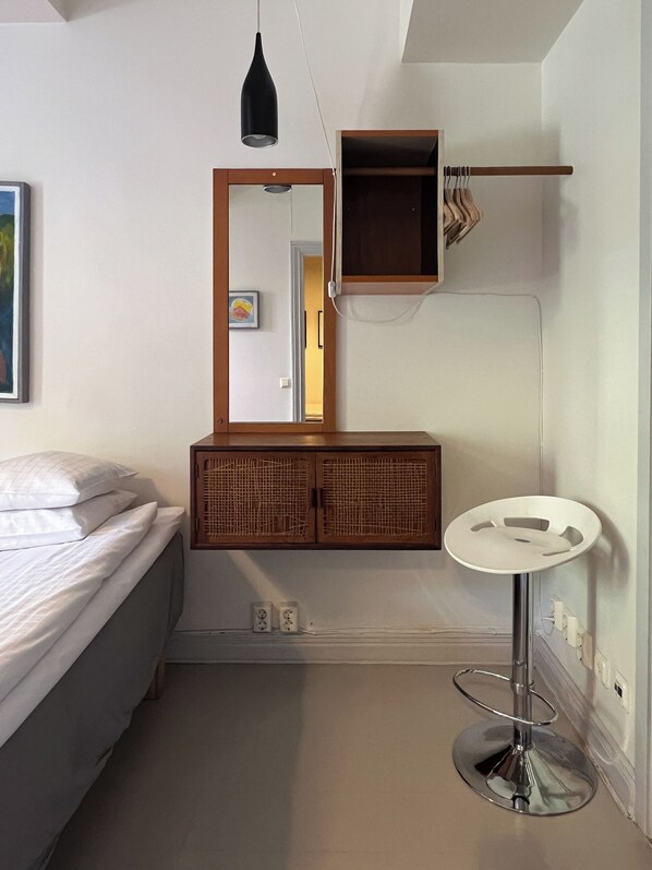 A bedroom with a bed, a bedside table, a mirror, a wardrobe, and a small round table with a stool.