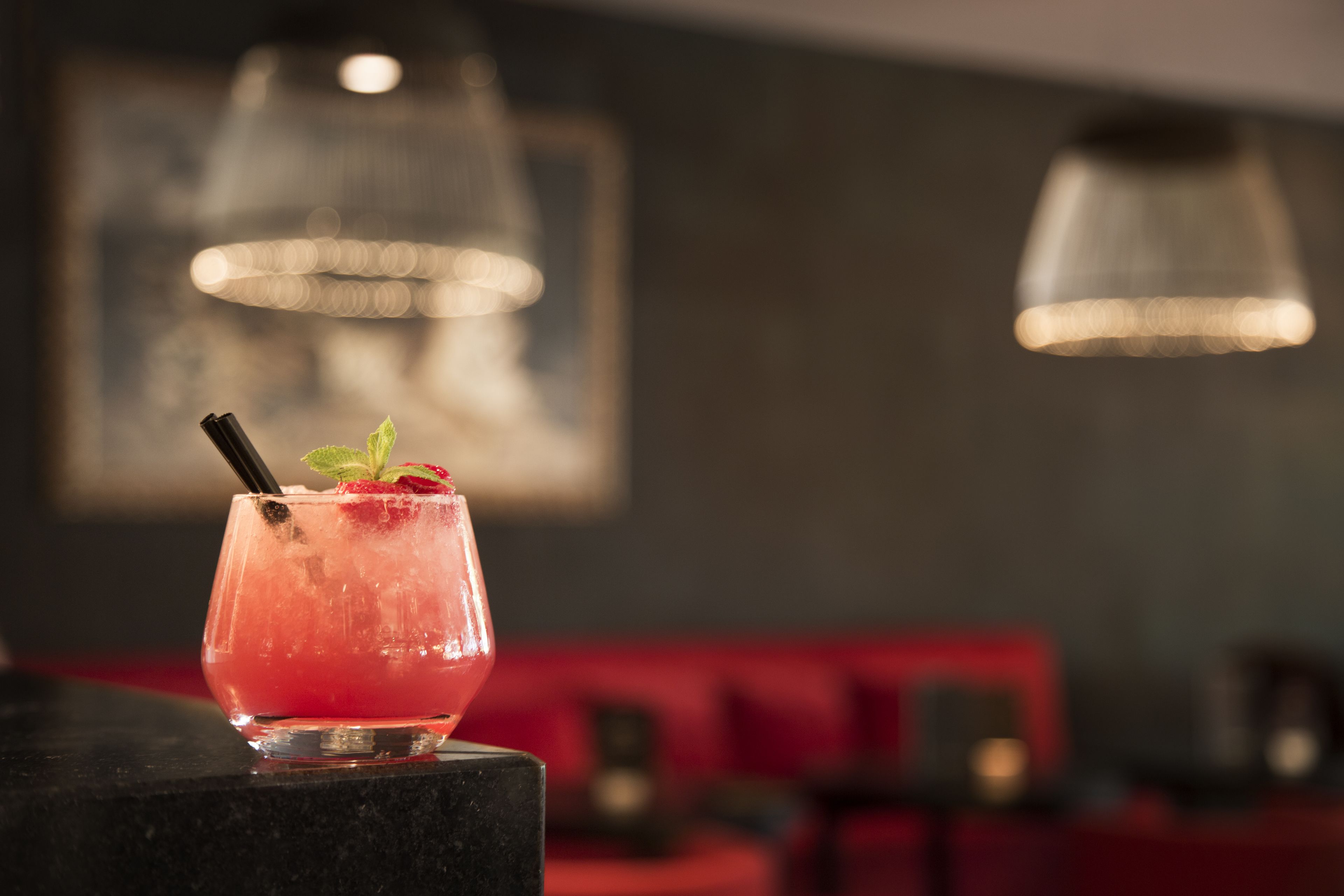 A cocktail in a glass with a straw and mint garnish on a bar counter.