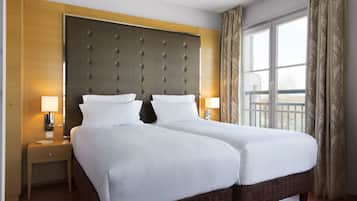 Habitación de hotel con una cama grande, dos mesitas de noche, un cabecero y una ventana con cortinas.