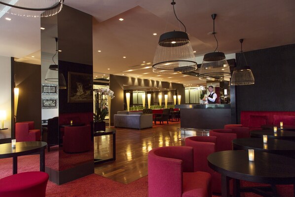 A modern hotel lobby with red seating, a bar area, and a reception desk.