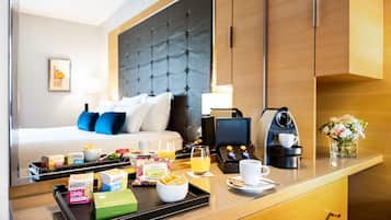 Una habitación de hotel con cama, mesita de noche y bandeja de desayuno con comida y bebidas.