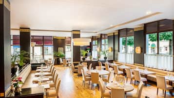 Un restaurante espacioso con techos altos, ventanas amplias y diferentes opciones de asientos, incluyendo cabinas y mesas.