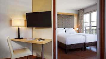 Una habitación de hotel con una cama, un escritorio con silla, televisión y ventana con cortinas.