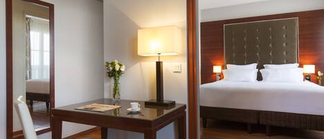 A hotel room with a bed, bedside lamps, a table with a cup and flowers, a chair, and a mirror.