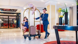 A hotel lobby with a modern interior, a luggage cart with a teddy bear, and a person in uniform. - Relais Spa Val d'Europe (Chessy)