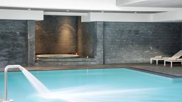 Piscina interior moderna com um recurso aquático, paredes de pedra e espreguiçadeiras.