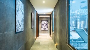 A hallway with tiled floors, framed artwork on the walls, and a large window on the right. - Relais Spa Val d'Europe (Chessy)