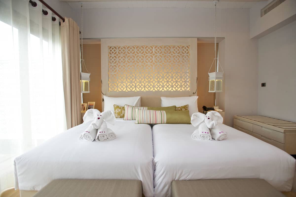 A hotel room with two beds, a decorative screen, bedside lamps, and towels on the beds.