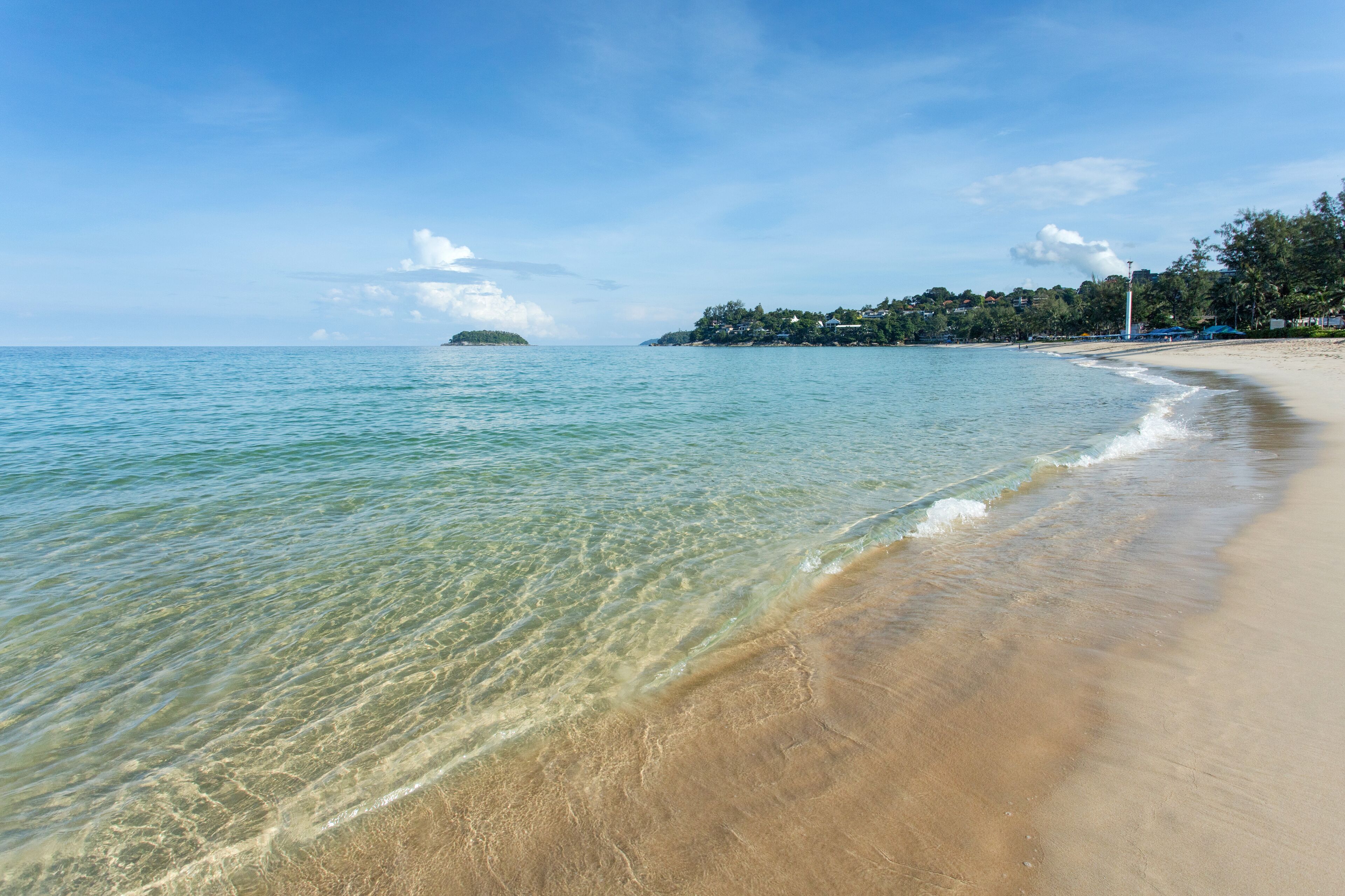 A beach with clear water, a sandy shore, and a distant island.