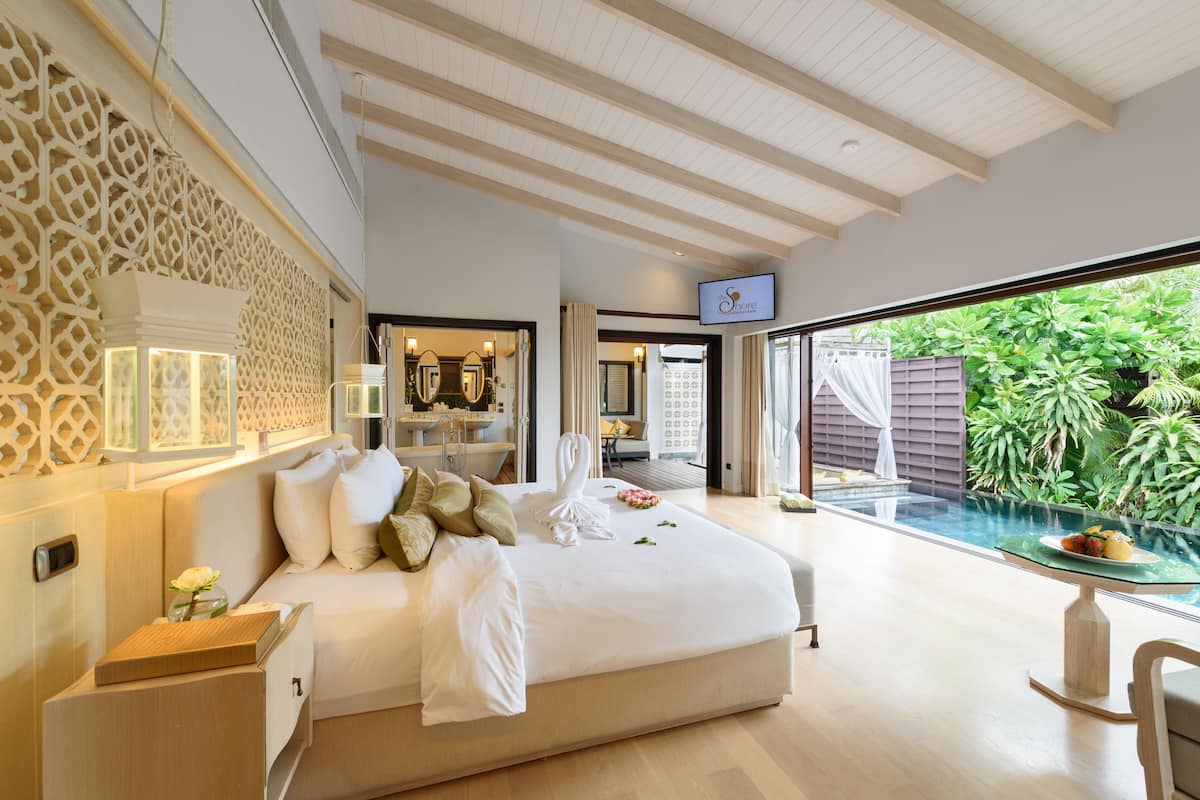A spacious bedroom with a large bed, a glass table with a view of the garden, and a TV mounted on the wall.