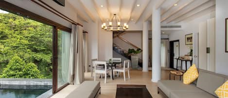 A spacious living room with a large window, a staircase, and a pool view.