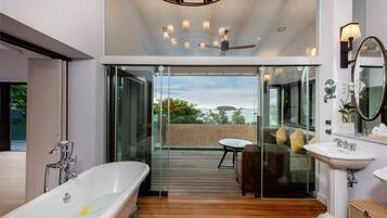Un baño moderno con una bañera independiente, zona de ducha con mampara de vidrio y terraza de madera que conduce a un balcón con vista al mar.