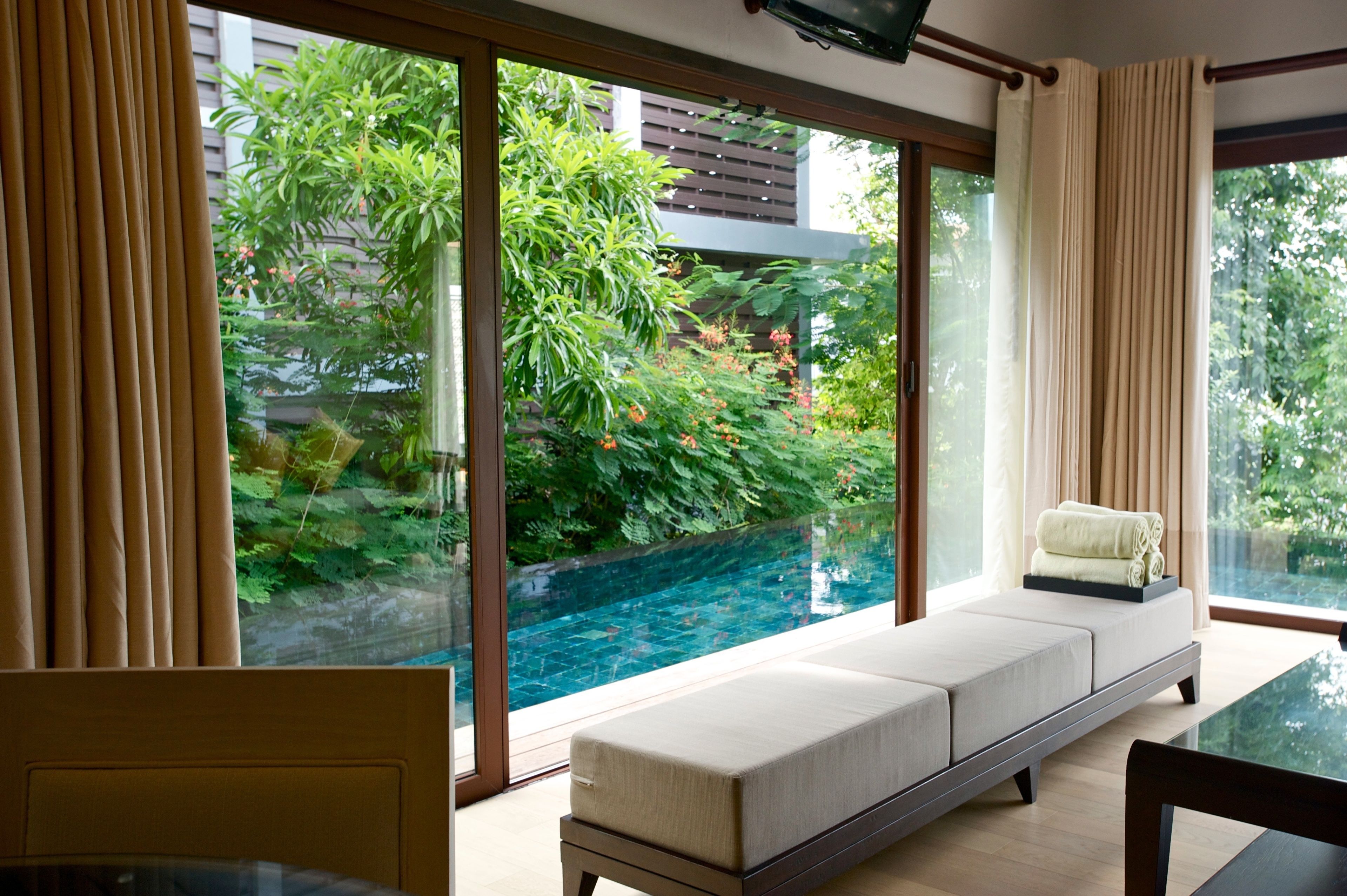 Habitación moderna con pared de vidrio que da a una piscina, un rincón de descanso con cojines y una mesa de comedor.