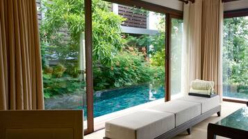 Habitación moderna con pared de vidrio que da a una piscina, un rincón de descanso con cojines y una mesa de comedor.