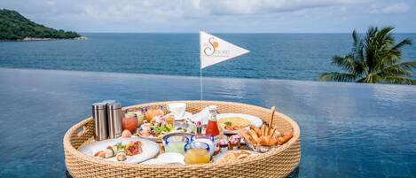 A floating breakfast setup with a flag, surrounded by a body of water with a view of the sea and a palm tree.