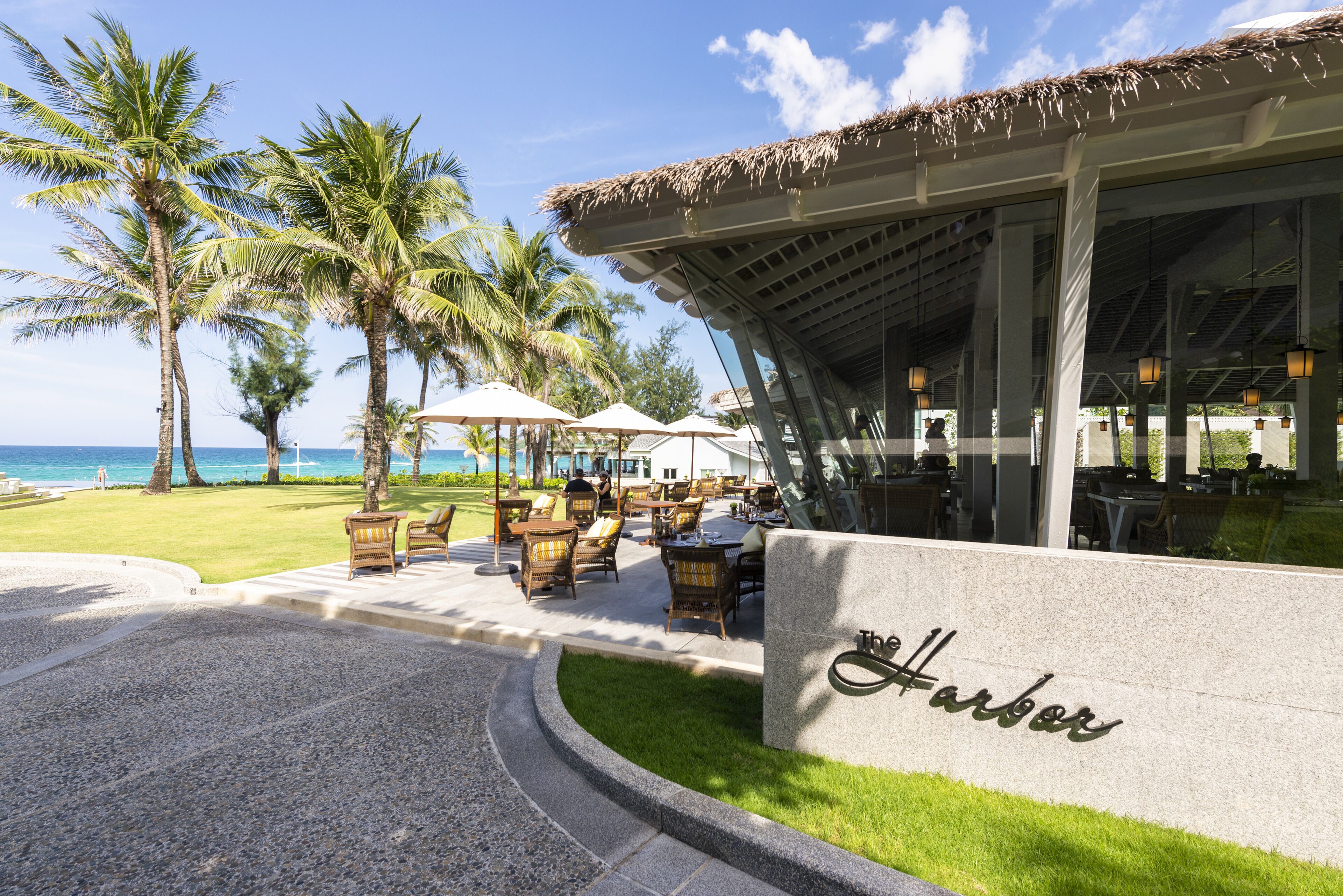 A beachfront restaurant with outdoor seating, palm trees, and a view of the ocean.
