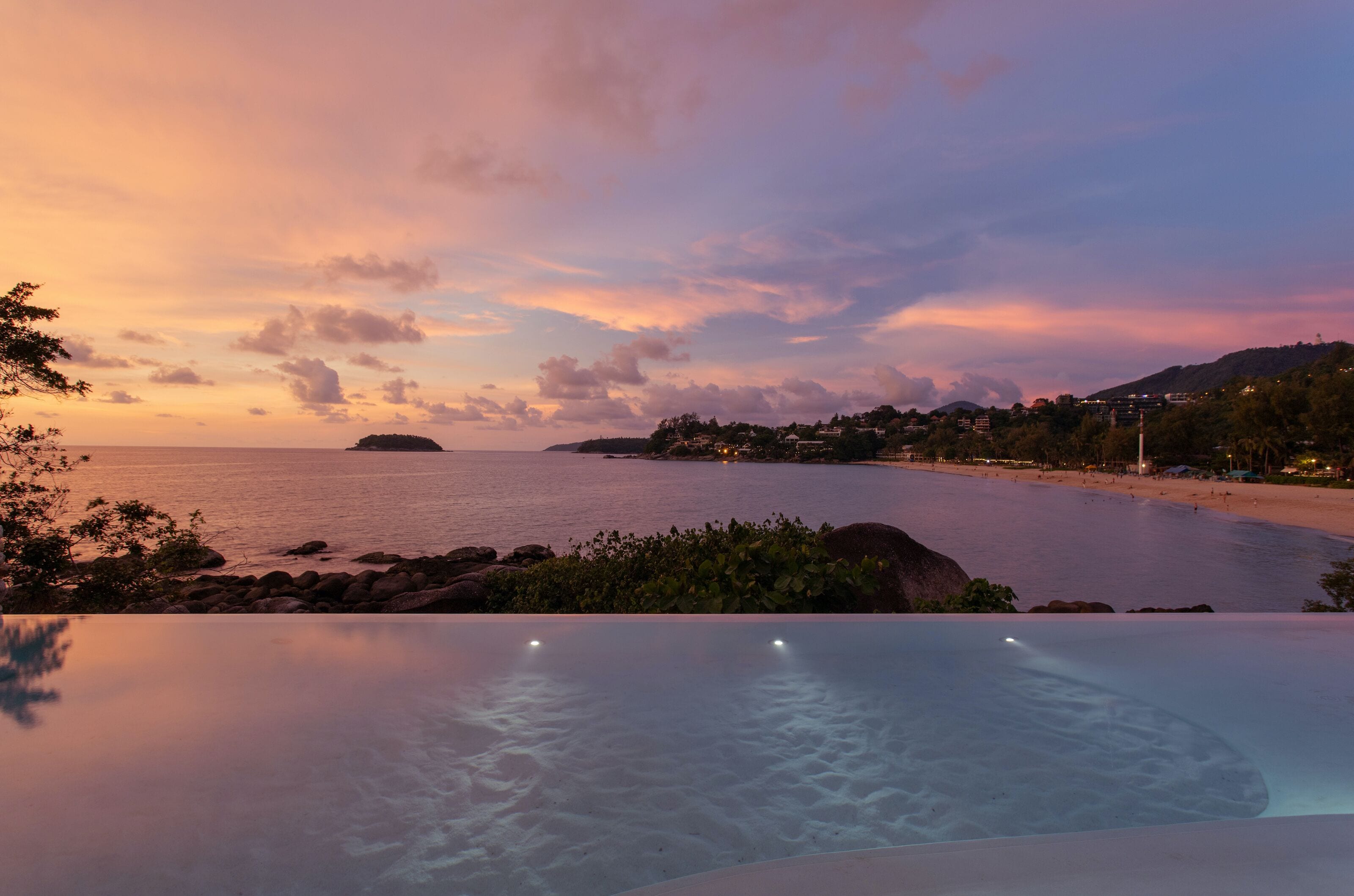 A sunset view over a beach with an infinity pool in the foreground.