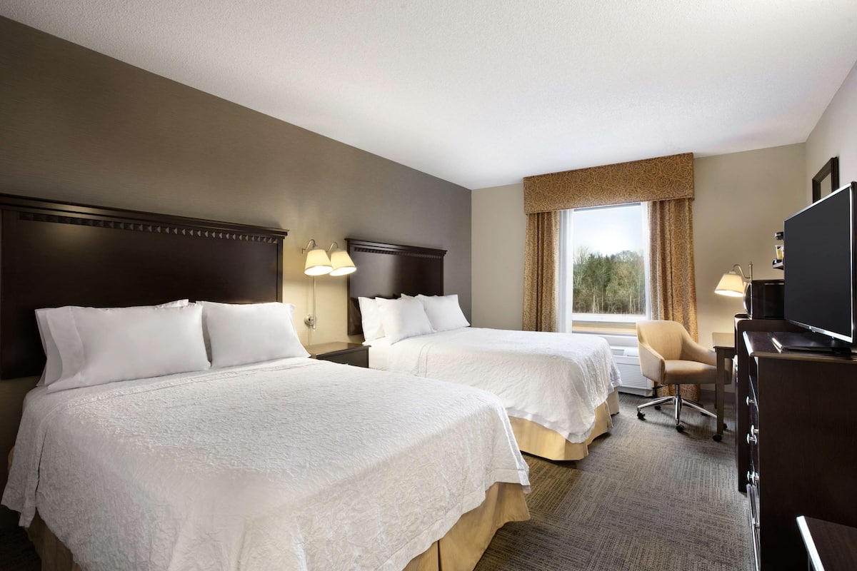 A hotel room with two beds, a desk, a TV, and a window with curtains.