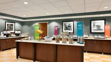 A well-lit, modern breakfast area with a central counter, various food items, and informational posters on the walls.